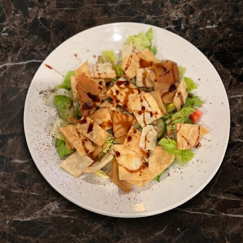 A white plate of fresh green salad with crispy pita bread and balsamic glaze on a marble table.