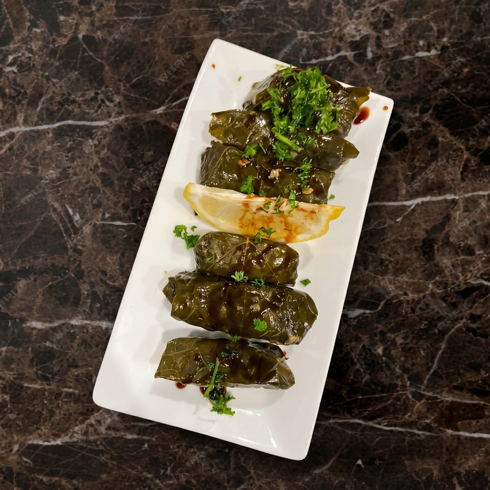 Dolmades, grape leaves stuffed with rice and herbs, garnished with parsley and lemon on a white plate.
